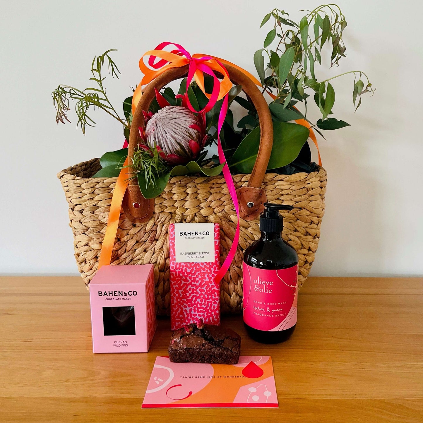Mother's Day gift basket featuring a woven basket, delicious chocolate brownie, bath products, and flowers.