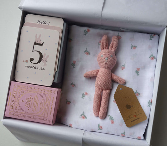 Sugar and Spice Baby Girl gift hamper featuring milestone cards, floral muslin wrap, and plush pink rabbit.
