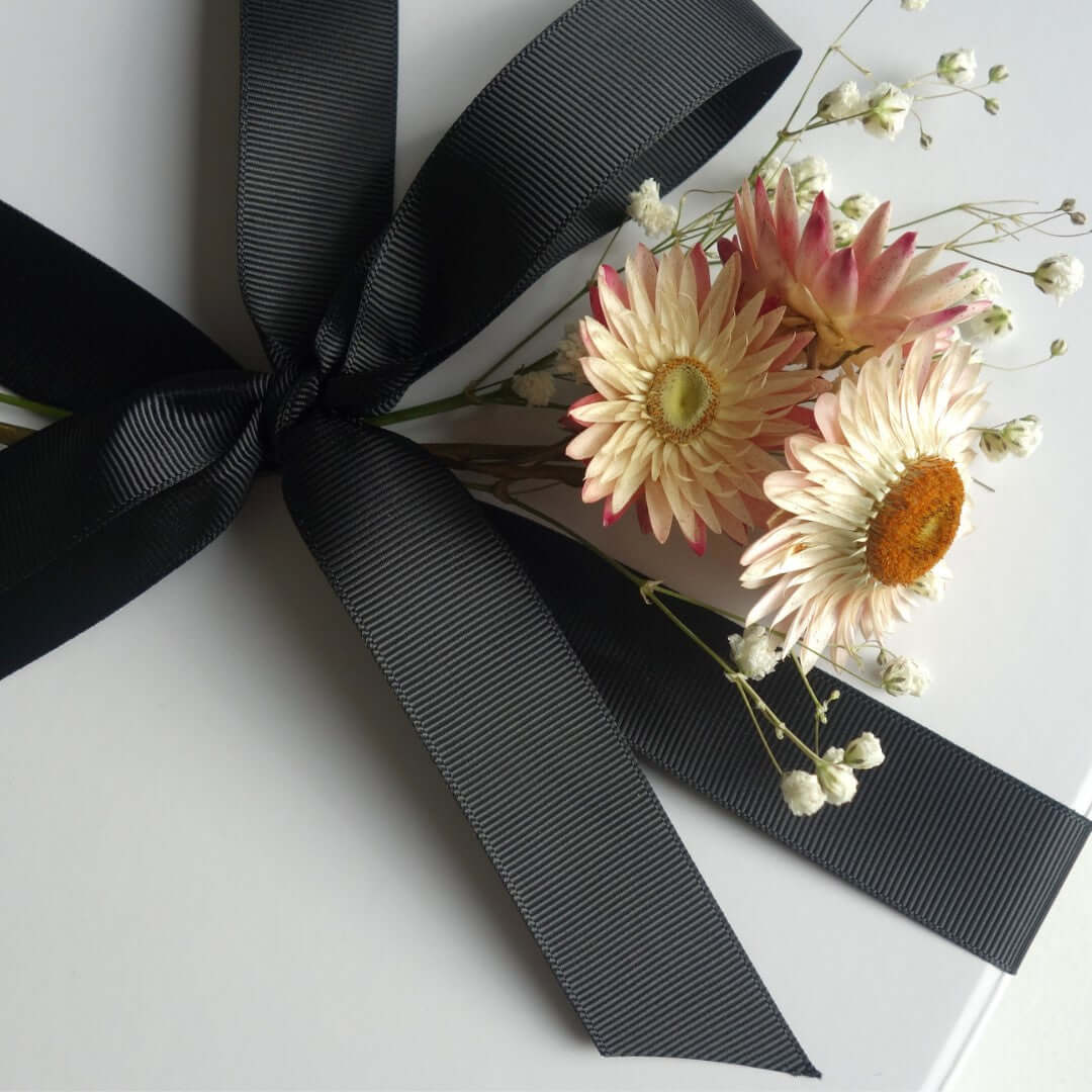 Black ribbon tied around a gift box decorated with dried flowers, perfect for a female self care gift box.