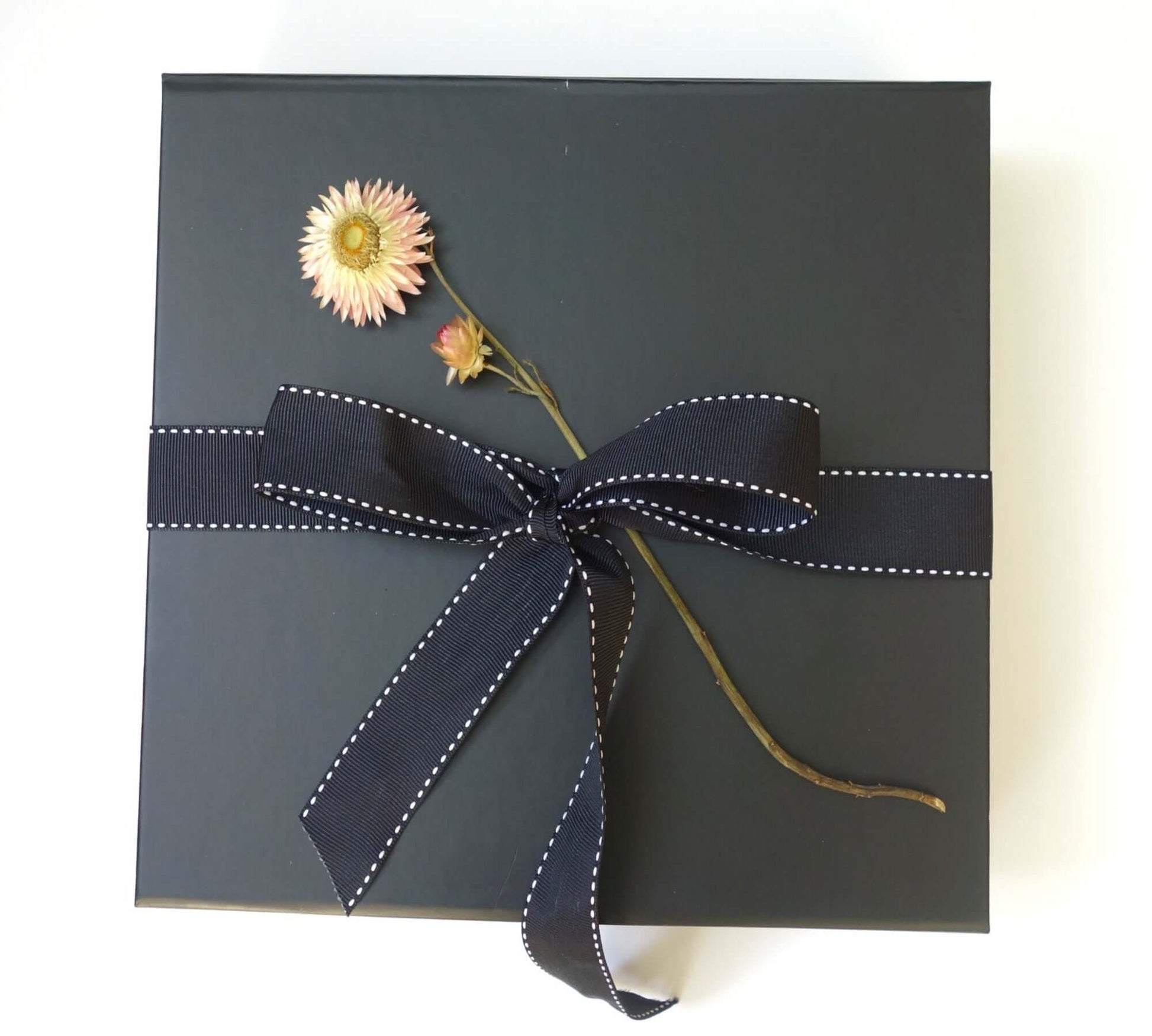 Indulgence black gift box with a floral decoration and navy ribbon for a luxury pampering experience.
